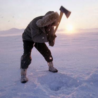 A man hacks through ice on Lake Hazen to fish for Arctic Char.